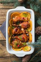 Baked chicken drumstick with oranges and cranberries in a baking sheet on a wooden background. Christmas food Table with decorations. photo