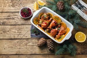 Baked chicken drumstick with oranges and cranberries in a baking sheet on a wooden background. Christmas food Table with decorations. Copy space. photo