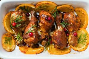 Baked chicken drumstick with oranges and cranberries in a baking sheet on a wooden background. Christmas food Close up photo