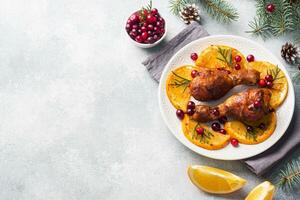 Baked chicken drumstick with oranges and cranberries in a plate light grey background. Christmas food Table with decorations. Copy space. photo