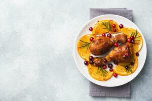 Baked chicken drumstick with oranges and cranberries in a plate light grey background. Christmas food Table with decorations. Copy space. photo