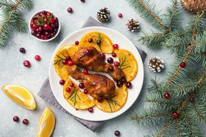 Baked chicken drumstick with oranges and cranberries in a plate light grey background. Christmas food Table with decorations. photo