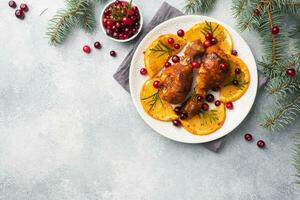 Baked chicken drumstick with oranges and cranberries in a plate light grey background. Christmas food Table with decorations. Copy space. photo