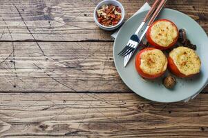 Baked whole tomatoes stuffed with mushrooms and cheese with seasonings on a wooden background. Copy space. photo