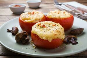 Baked whole tomatoes stuffed with mushrooms and cheese with seasonings on a wooden background. Close up Selective focus photo