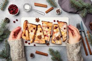 Female hands hold a stand with a Cottage cheese pie casserole with cranberries and spices sprinkled with powdered sugar. Gray concrete table. photo