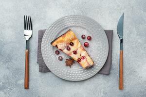 A piece of cottage cheese pie casserole with cranberry berries and spices cinnamon and anise on a plate. Grey concrete background. Copy space. photo