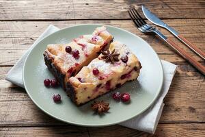 Two pieces of cottage cheese pie casserole with cranberry berries and spices cinnamon and anise on a plate. Wooden background. Copy space. photo