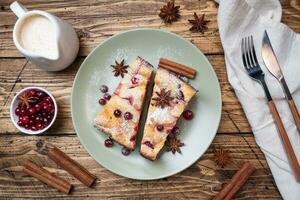 Two pieces of cottage cheese pie casserole with cranberry berries and spices cinnamon and anise on a plate. Wooden background. photo