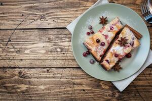 Two pieces of cottage cheese pie casserole with cranberry berries and spices cinnamon and anise on a plate. Wooden background. Copy space. photo