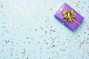 Flat lay background for celebration Christmas and New Year. Gift boxes are purple with gold ribbons bows and confetti stars on a blue background. top view copy space. photo