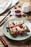 Two pieces of cottage cheese pie casserole with cranberry berries and spices cinnamon and anise on a plate. Wooden background. photo