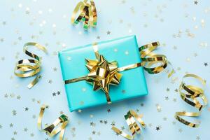 Flat lay background for celebration Christmas and New Year. Gift box turquoise with gold ribbons bows and confetti stars on a blue background. top view copy space. photo