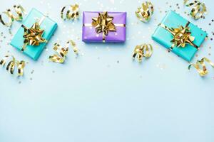 Flat lay background for celebration Christmas and New Year. Gift boxes are purple and turquoise with gold ribbons bows and confetti stars on a blue background. top view copy space. photo