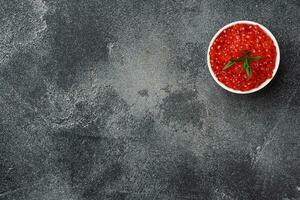 Red salmon caviar in a plate on a dark concrete background. Copy space. Snack delicacy. photo