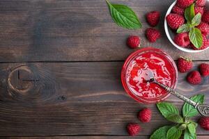 Homemade raspberry jam in a glass jar and fresh raspberries with mint on a wooden rustic background. Copy space photo