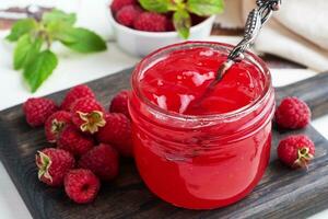 Homemade raspberry jam in a glass jar and fresh raspberries with mint on a wooden rustic background. Close up. photo