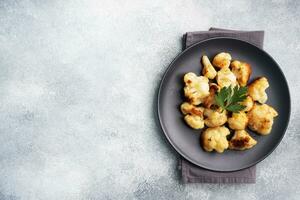 Fried cauliflower florets in batter on a black plate. Grey concrete background. Copy space. photo