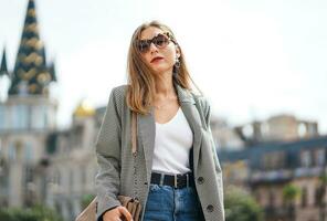 Tired woman walks down street. City background of beautiful architectural buildings. Strict businesswoman wearing jacket and jeans walking around the square. Sunny summer day. Blurred background. photo