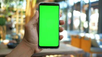 mano de hombre joven usando un teléfono inteligente con pantalla verde en el café video