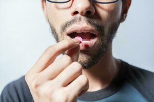 Person taking a pill isolated, Close up of young man putting a pill in his mouth. Self-medication concept, Man putting a pill in his mouth isolated, Close-up of a man taking an aspirin photo