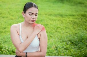 Young woman with shoulder pain sitting outside. Girl suffering from shoulder pain sitting outdoors. Woman sitting and stressed with shoulder pain outdoors. Girl with shoulder pain outdoors photo