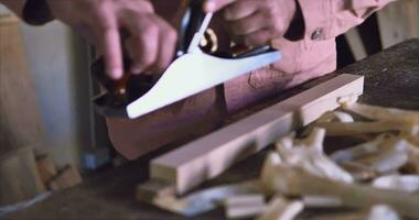 A carpenter in a red jacket works with a large hand plane. Shows fine shavings. The video has high-quality sound
