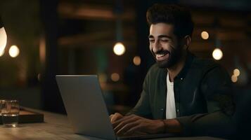 Cheerful bearded man using laptop while sitting in cafe at night photo