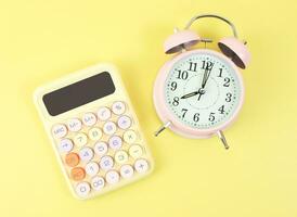 flat lay of colorful calculator and pink alarm clock 8 o clock on yellow background. photo