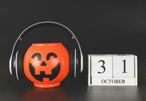 calabaza de halloween de plástico cubierta con auriculares, aislada sobre fondo negro con calendario de madera el 31 de octubre. música de halloween, audio, fiesta. foto