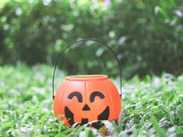 plastic halloween pumpkin figure basket on green grass  in the garden. Jack o'lantern basket, halloween decoration trick or treat concept. photo