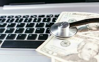 Medical cost concept. Stethoscope on top of money on laptop keyboard. Stethoscope on dollar bills on top of laptop keyboard photo