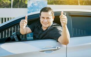 Happy driver giving a thumbs up on the road. safe driving concept. Satisfied driver man showing thumb up. Young driver man in the car showing thumb up photo