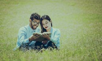 Two people sitting on the grass reading a book, concept of people reading outside, A couple sitting on the grass reading a book photo