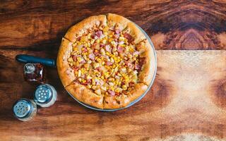 Top view of ham and corn pizza on wooden table. Ham pizza with corn on wooden background photo