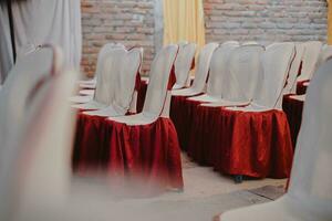 chairs with red and white sashes are lined up in a room photo