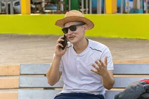 un atractivo chico vocación en un célula teléfono en un banco, un hombre sentado en un banco vocación en el teléfono. foto