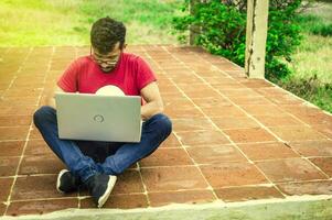 Concept of person sitting on the floor typing on his laptop, Side view of student man sitting cross-legged on the floor with his laptop, Teenage student sitting on the floor working on laptop photo