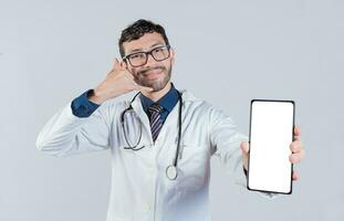 Handsome doctor showing cellphone screen gesturing call me. Happy doctor showing white screen of cellphone photo