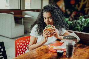 Portrait of afro girl holding a hamburger in a restaurant. Beautiful latin girl enjoying a delicious hamburger in a restaurant photo