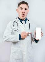 Shocked doctor pointing an application on the cell phone. Amazed young doctor holding and pointing cell phone screen photo