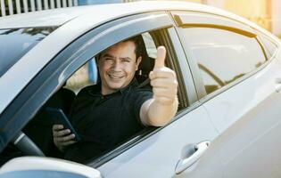 Smiling driver holding cellphone showing thumb up. Driver man showing thumb up while holding cellphone. Happy driver giving a thumbs up on the road. safe driving concept photo