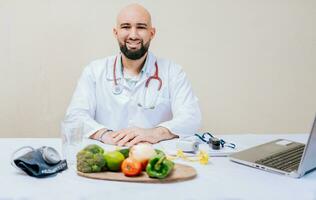 Portrait of smiling nutritionist at her desk. Smiling nutritionist doctor at desk with laptop and vegetables. Bearded nutritionist doctor at his workplace photo