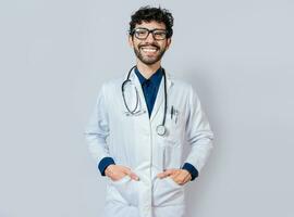 sonriente médico en aislado antecedentes. contento médico con manos en bolsillos retrato de sonriente joven médico aislado foto