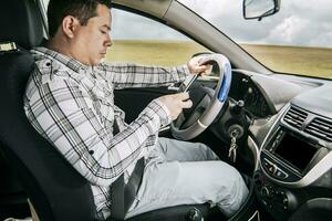Man sitting in his car texting with his cell phone, Side view of a young man sitting inside car using mobile phone, Young man sitting in a car and looking at a mobile phone photo