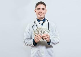 Latin young doctor holding money isolated. Cheerful doctor showing dollars isolated photo