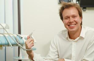 Laughing man with tousled hair holding dental tool photo