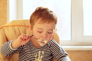 Two year old boy eats porridge in the morning. photo