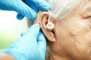 Doctor install hearing aid on senior patient ear to reduce hearing loss problem. photo