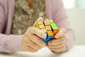 Bangkok, Thailand - May 15, 2022 Asian elderly woman playing Rubik cube game to practice brain training for help dementia prevention and Alzheimer disease. photo